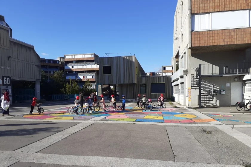 Une dizaine d'enfants se regroupent en vélo sur l'immense jeu de l'oie peint sur le sol de la place des Géants à Grenoble.