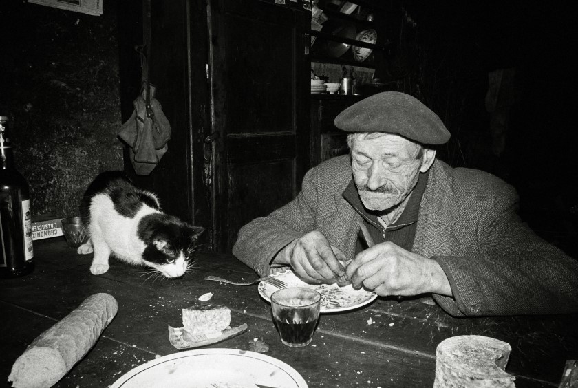 Un vieux monsieur dine en présence de son chat.