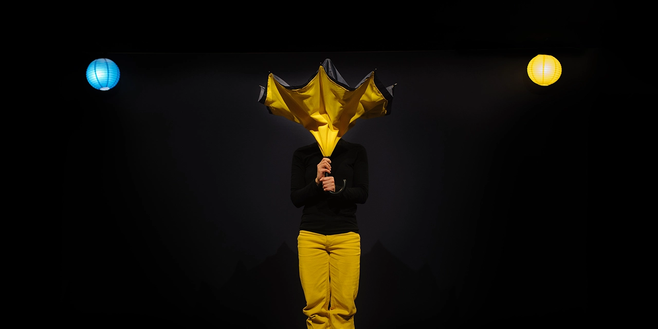 La comédienne Magali Benvenuti cache son visage derrière un parapluie jaune.