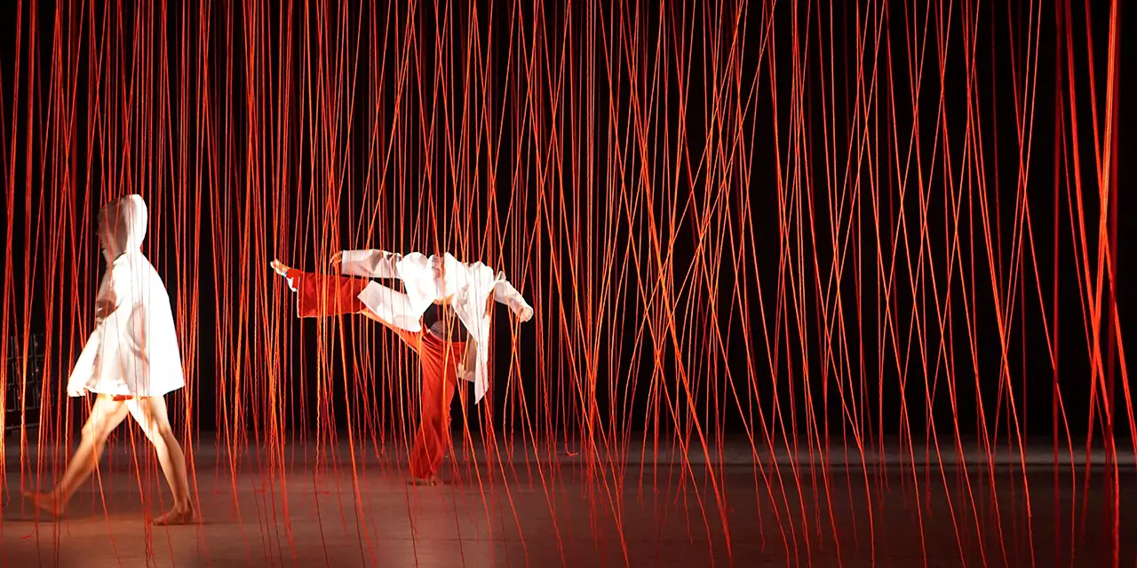 Deux danseuses sur scène avec des fils rouges suspendus comme scénographies