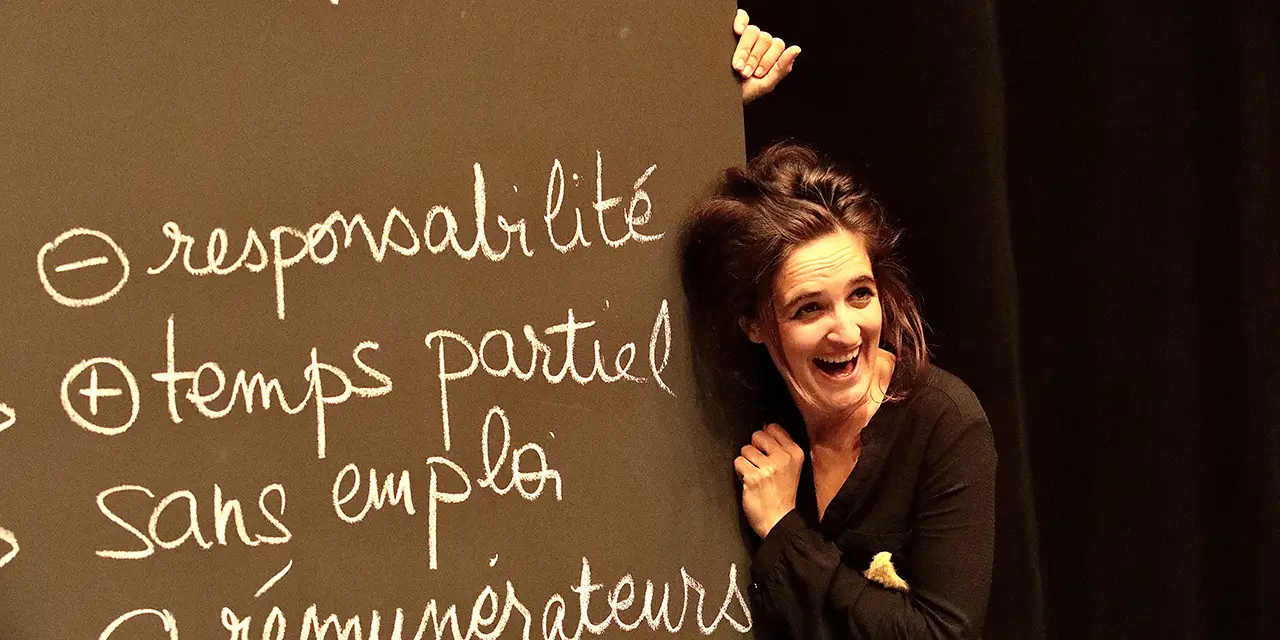 La comédienne Maëlle Mays en plein rire à côté d'un tableau d'école