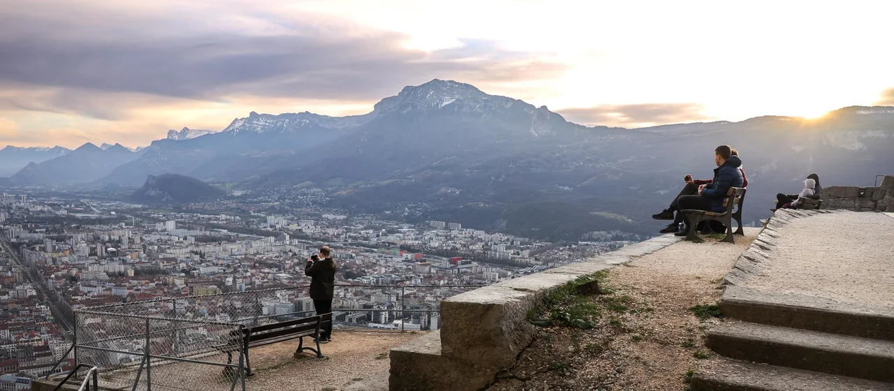 Des personnes en fin de journée regardent le coucher de soleil sur Grenoble depuis la Bastille.