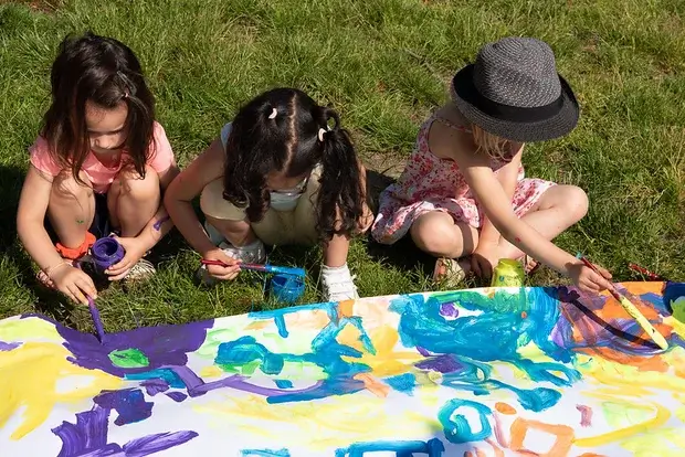 Trois petites filles font de la peinture sur une grande bâche.