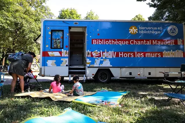 Photo du bibliobus dans le parc de la savane avec dex enfants lisants sur des tapis